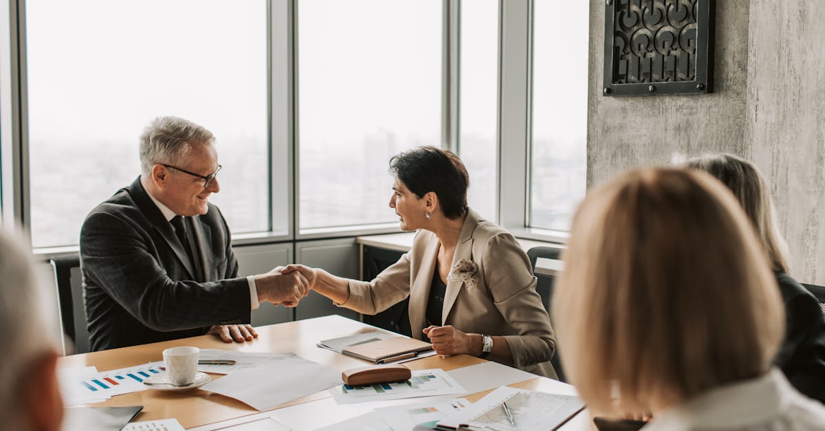 Colleagues in business attire shake hands during a formal meeting in a modern conference room.