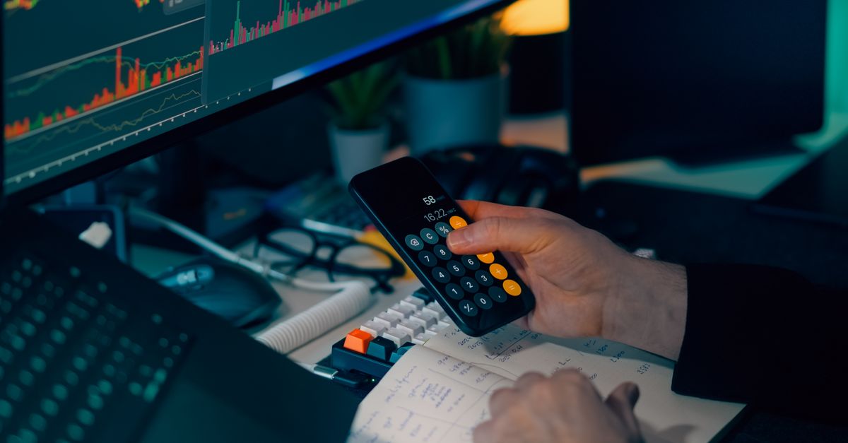 Business analysis with calculator and computer monitor displaying financial graphs and charts.