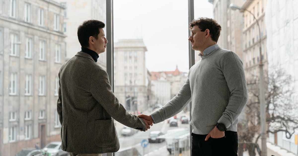 Two businessmen shaking hands in an urban office with city view through large windows.