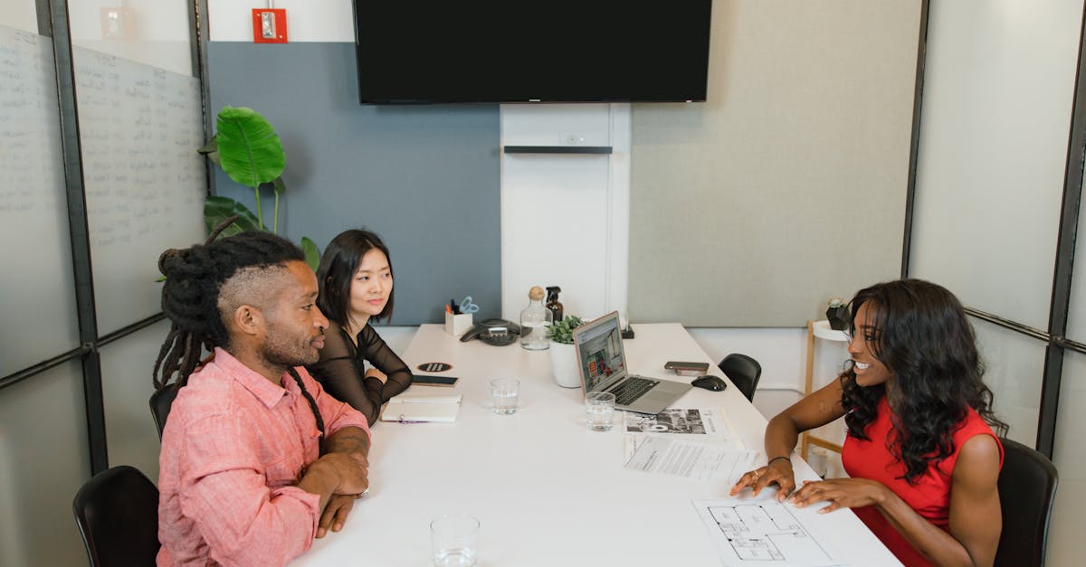 Three professionals engaged in a meeting around a white table in a modern office environment.