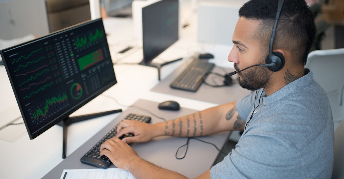 Man in a headset analyzing stock data on a computer monitor at his workspace.