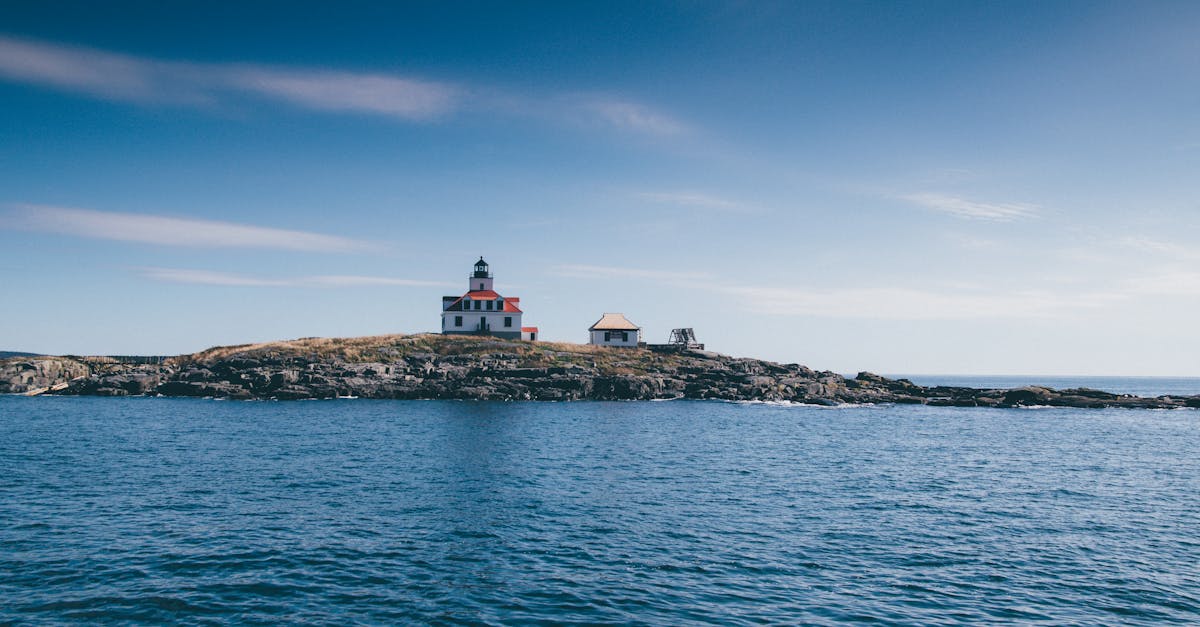 A picturesque lighthouse on a rocky island surrounded by the ocean under a clear blue sky.