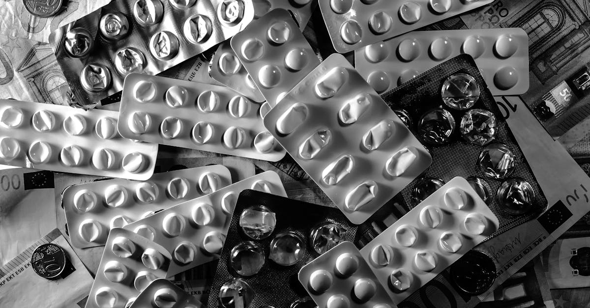 Black and white image of pill blister packs scattered on euro bills and coins.