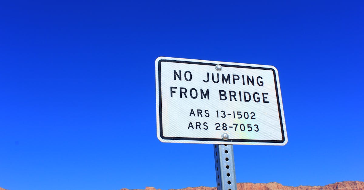 A warning sign stating 'No Jumping from Bridge' against a clear blue sky and rugged terrain.