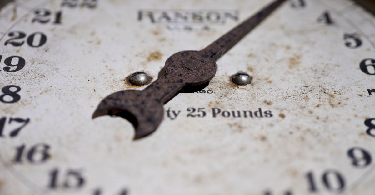 Close-up of an antique rusty weighing scale showing its weathered dial and numbers.