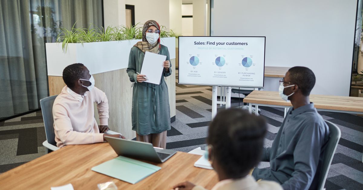 Colleagues wearing masks in a modern office discussing sales strategies.