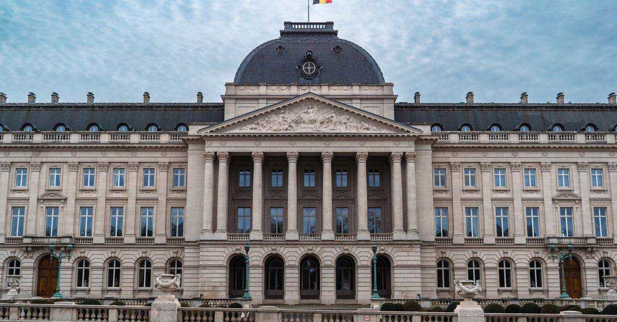 Front view of the Royal Palace of Brussels with Belgian flag under a cloudy sky.